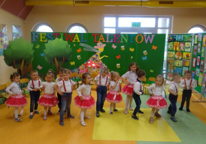 Dzieci tańczą ustawione w szeregu z rączkami na bioderkach, jedną nóżką tupią rytmicznie w podłogę.